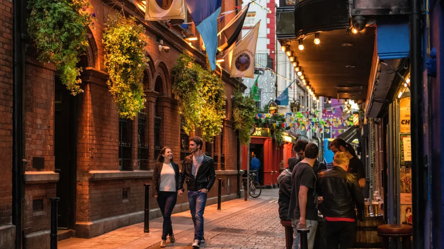 A smiling couple walking along Dublin’s Dame Lane beneath hanging baskets and lights