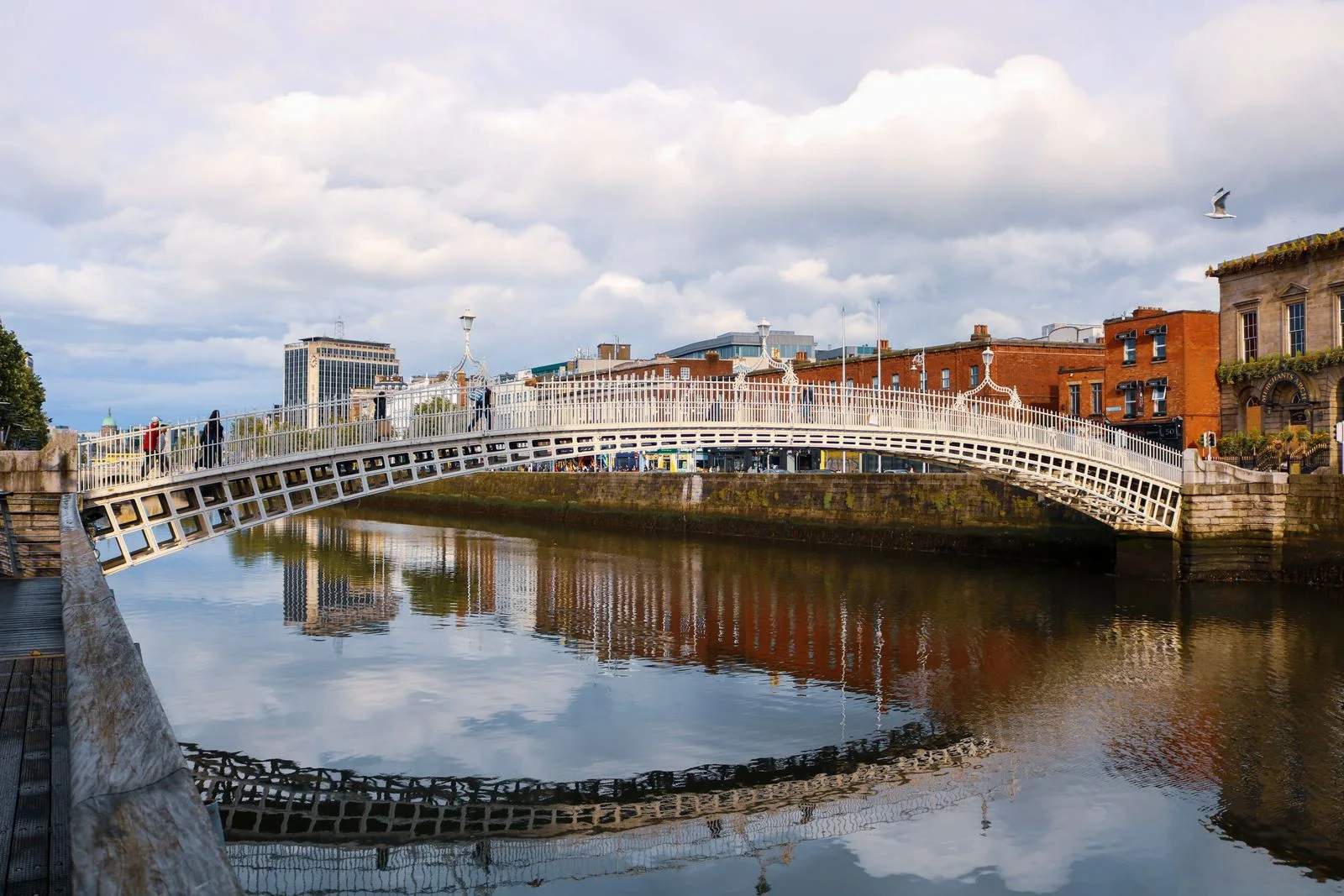 People crossing Ha’penny Bridge over the River Liffey, with Dublin’s colourful riverside buildings beyond