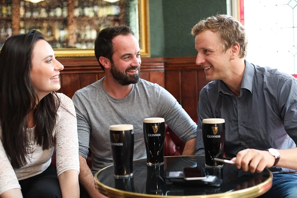 Three people smiling and chatting over pints of Guinness in a pub